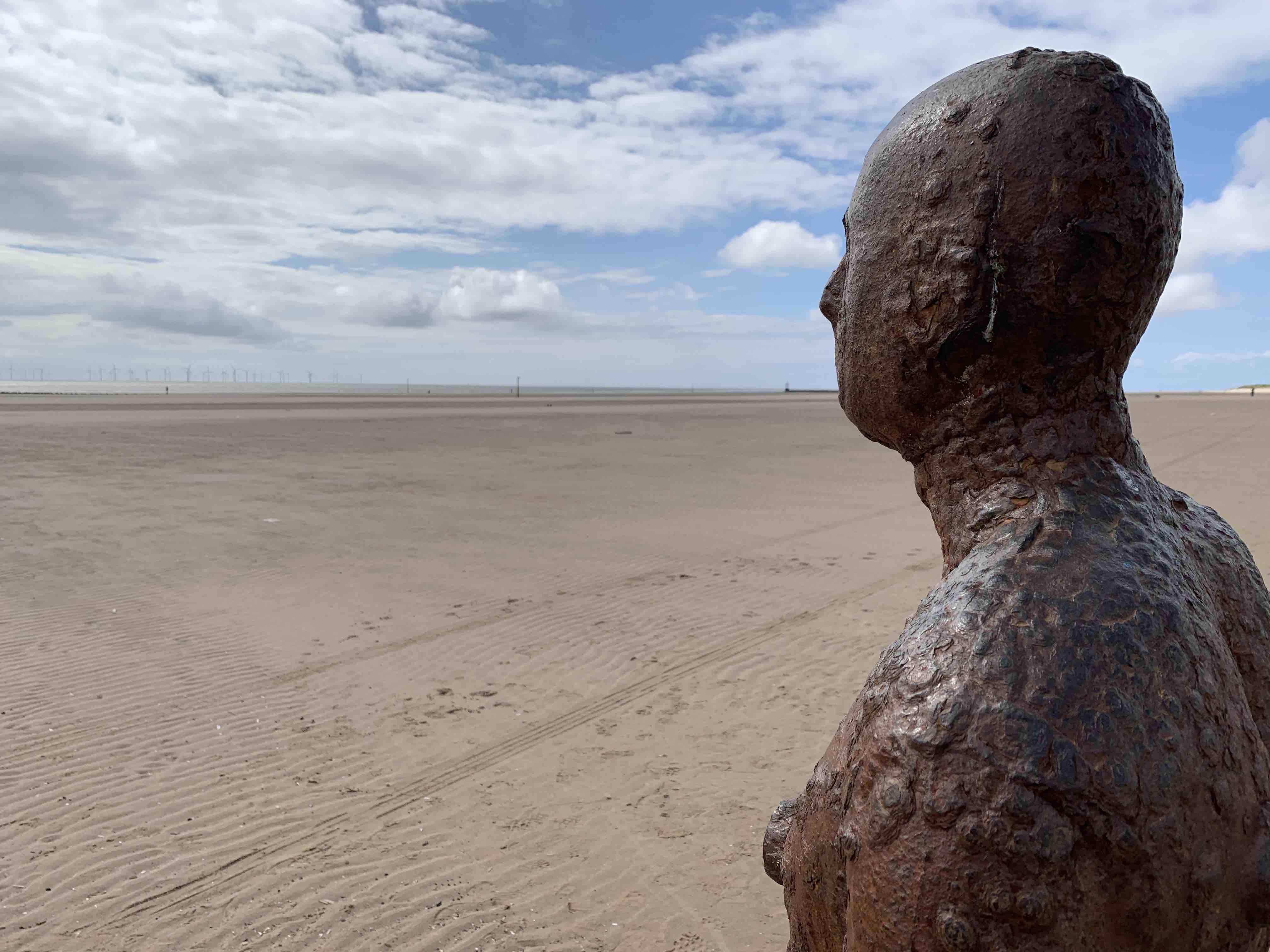 Over the shoulder, looking out to sea of the head and torso of one of The Iron Men of Crosby Beach installation, Liverpool